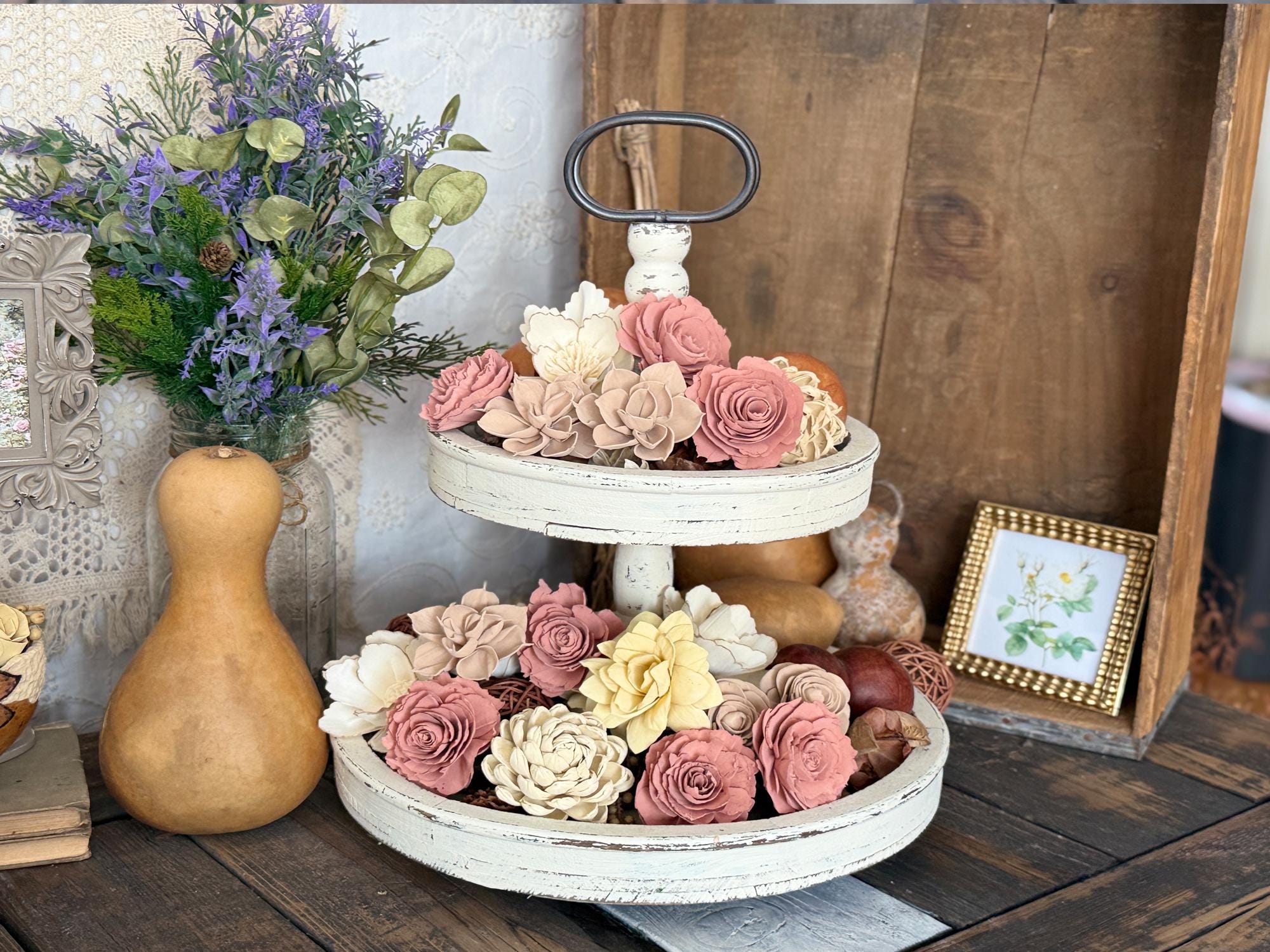 Decorative tiered tray with wood flowers on a wooden surface, surrounded by other decorative items.
