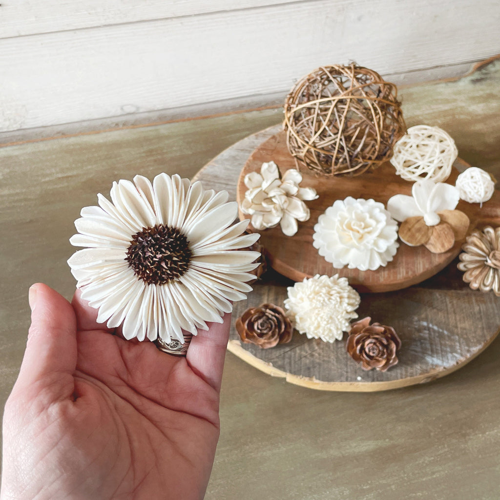 Hand holding a white flower-shaped object with a wooden surface and decorative items in the background.