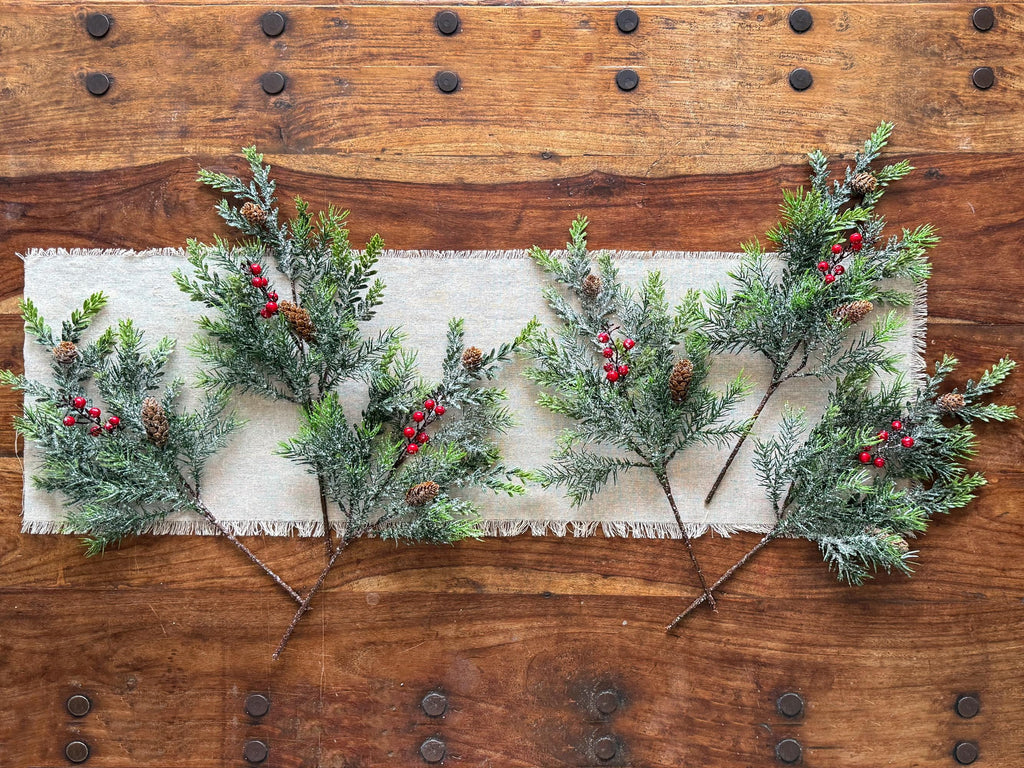 Decorative greenery with red berries on a white fabric runner against a wooden background