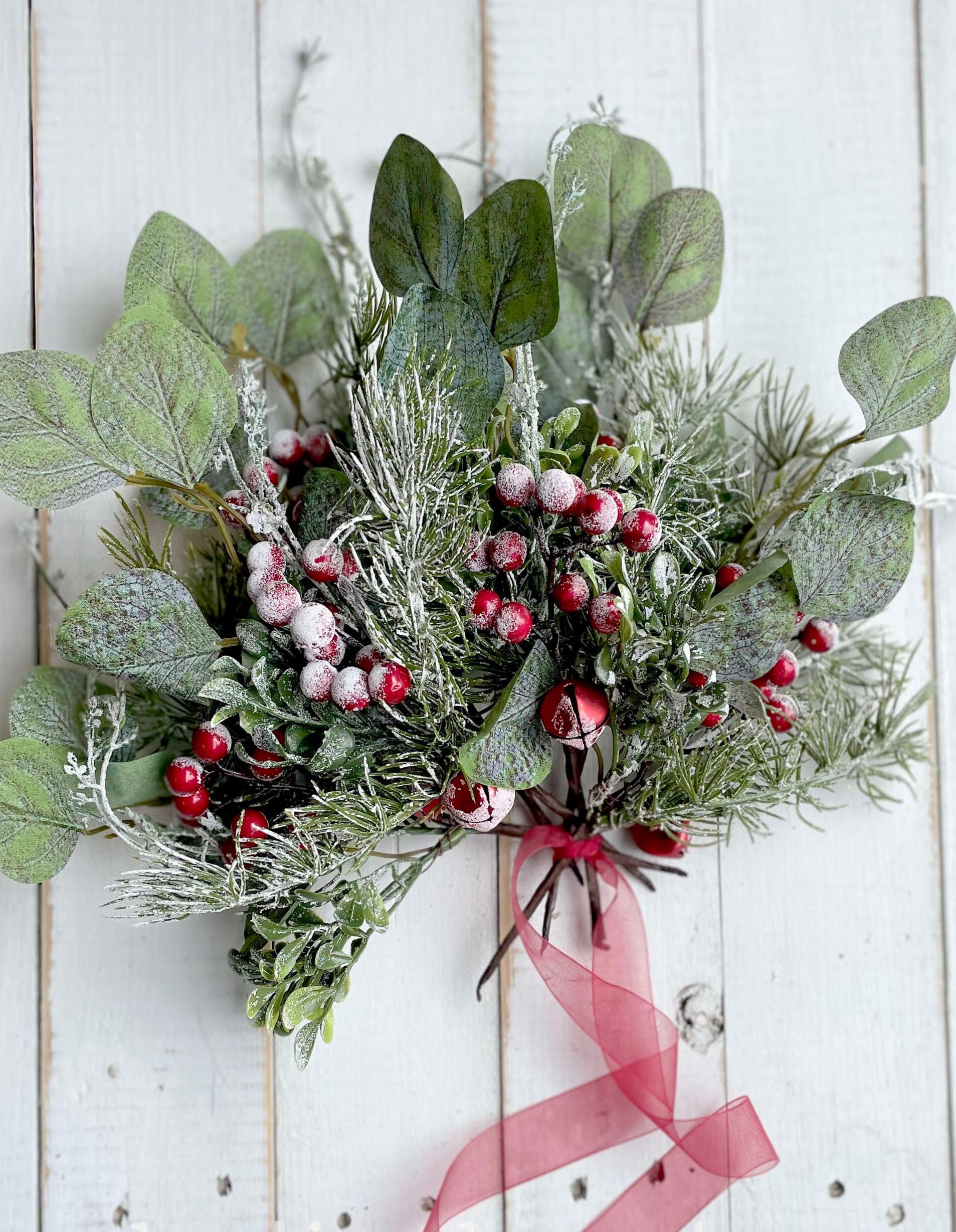 Decorative wreath with green leaves, red berries, and a pink ribbon on a white wooden background