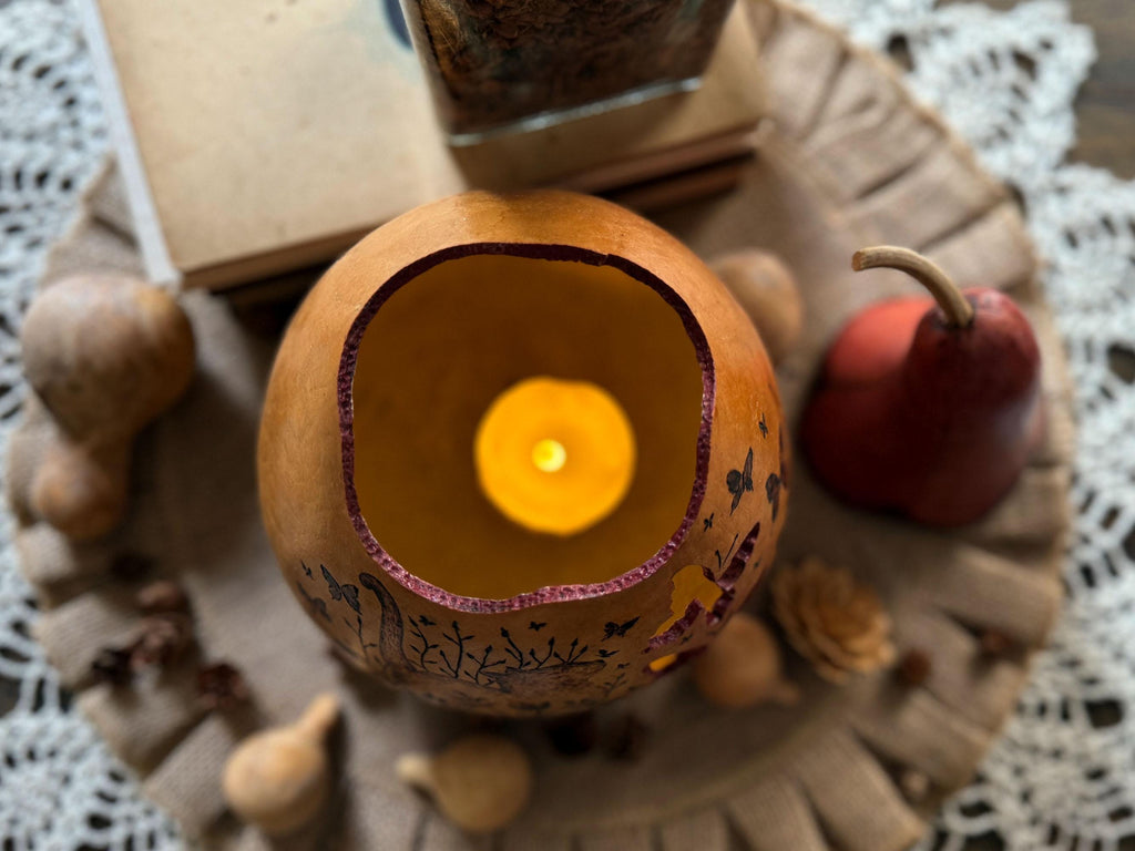 Candle inside a decorative gourd on a textured surface with autumn-themed items.