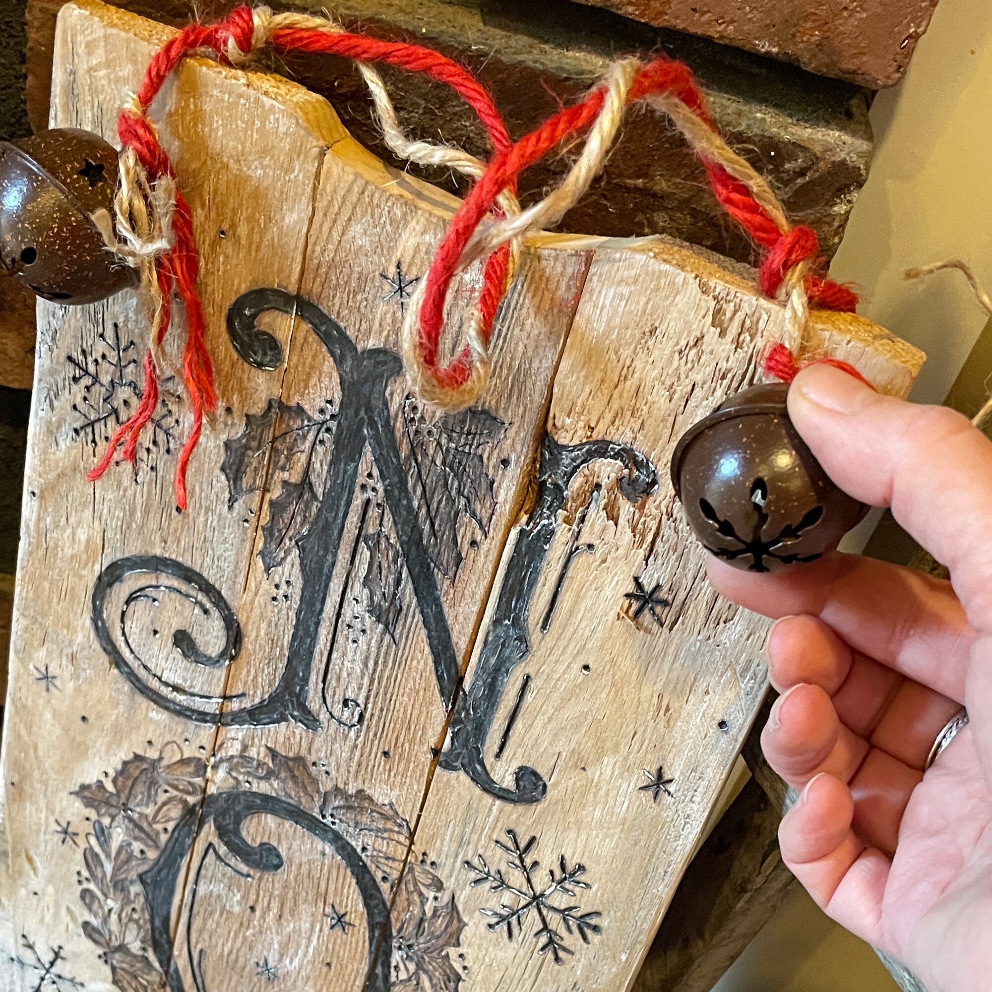 Wooden ornament with letter 'N' and decorative bells, held by a hand.