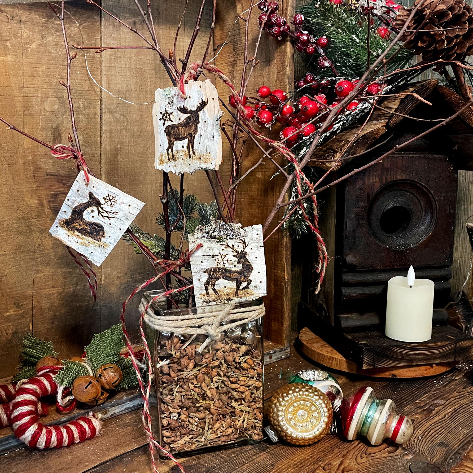 Decorative vase with branch bouquet, jars, candles, and festive elements on a wooden surface. White birch tags hang from branches.