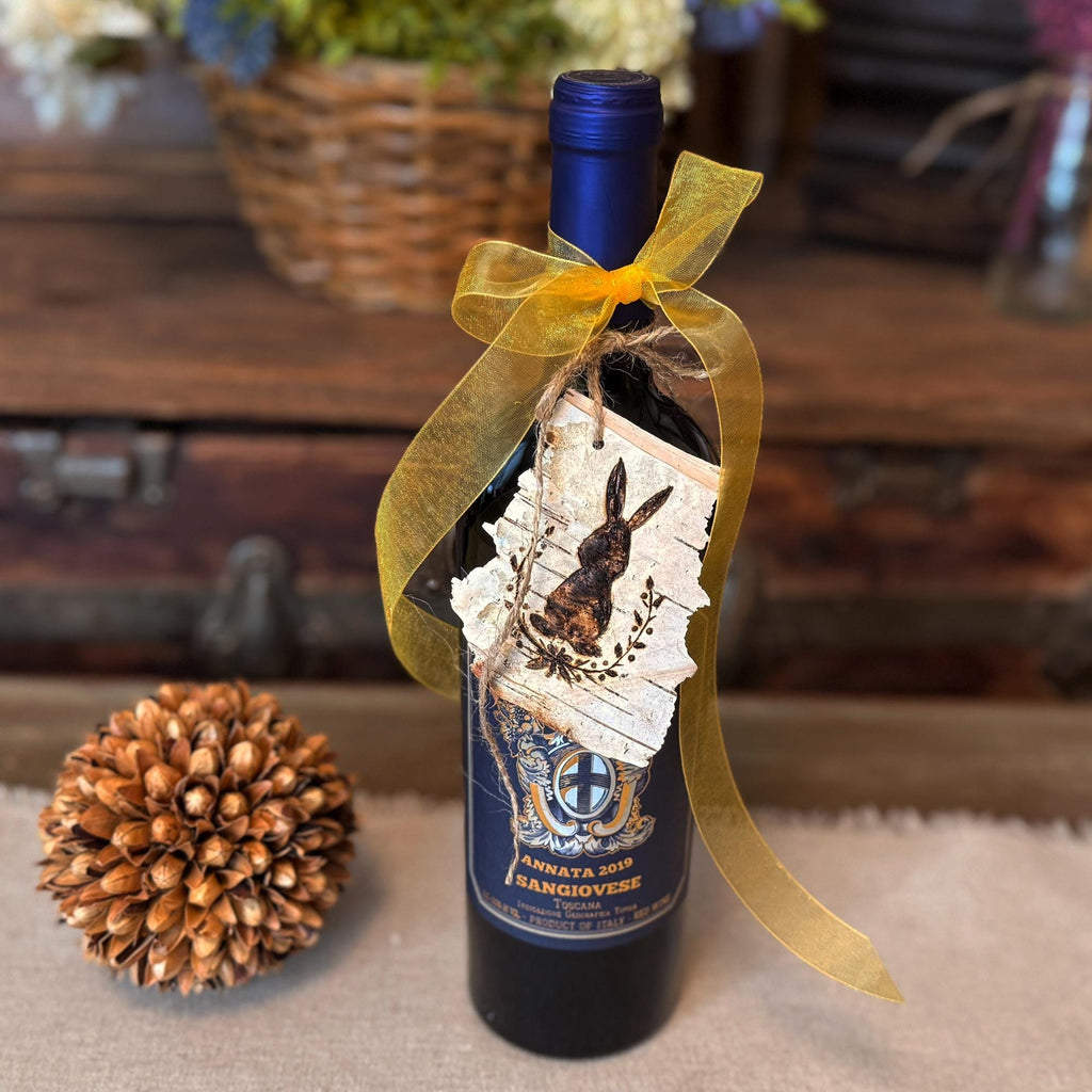 Wine bottle with decorative birch bark tag and yellow ribbon on a wooden surface