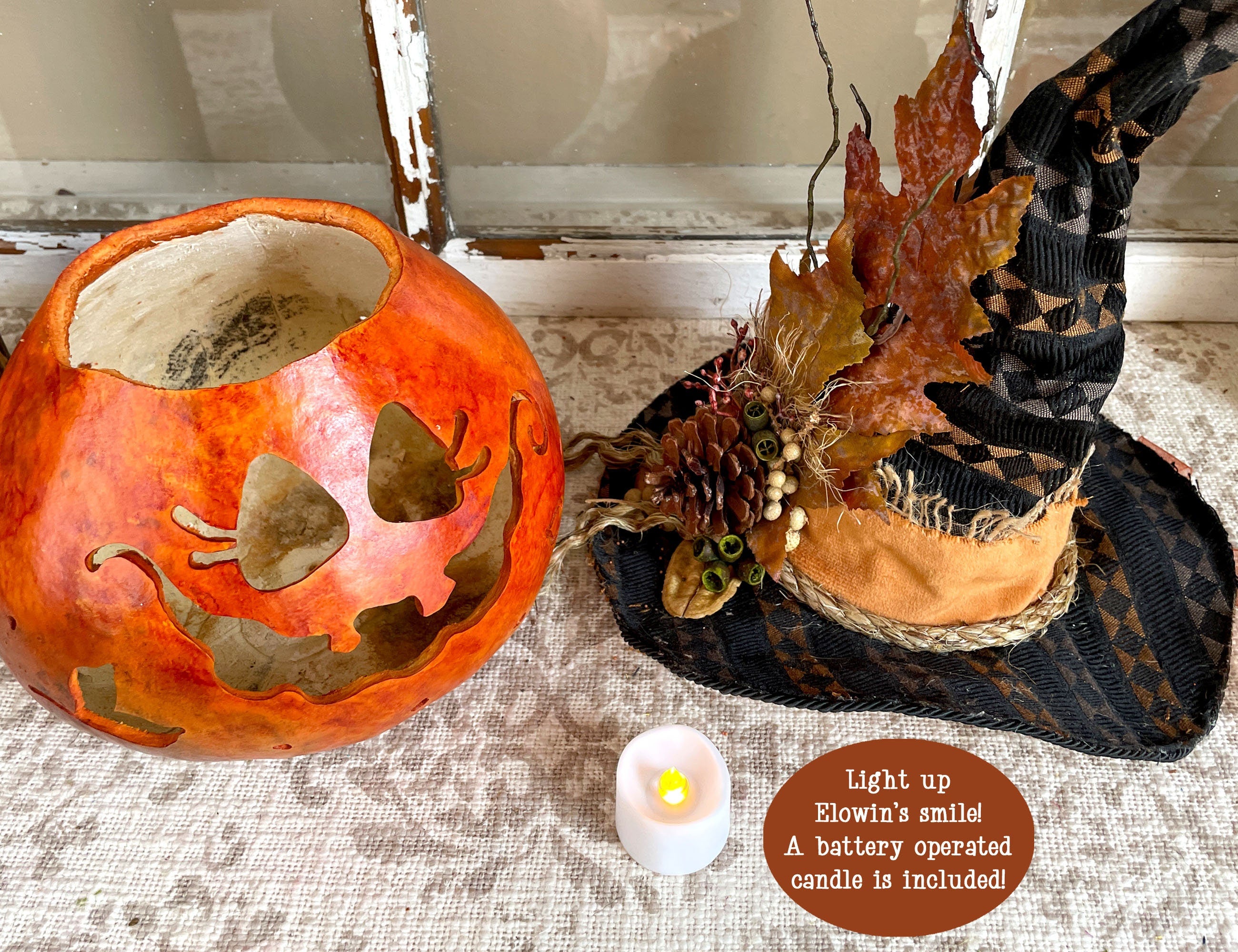 Decorative pumpkin with leaf patterns and a witch hat on a textured surface.