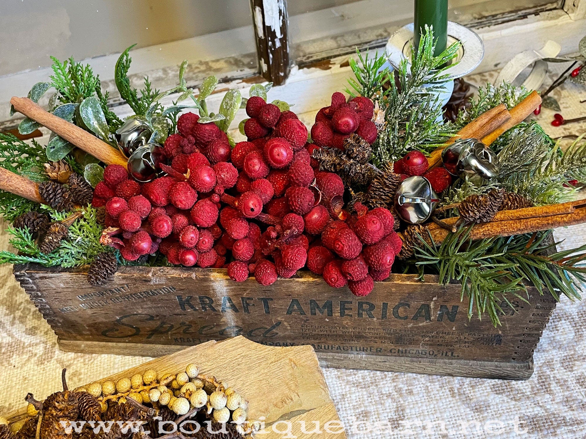 Decorative arrangement with red berries, greenery, and a wooden box labeled 'Kraft American' on a rustic surface.