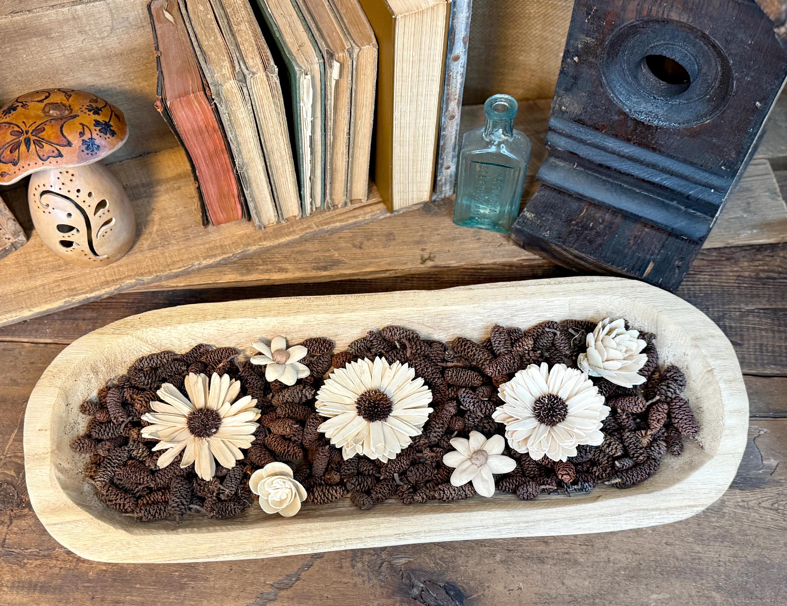 dough bowl with floral designs on a wooden surface with books and a bottle in the background.