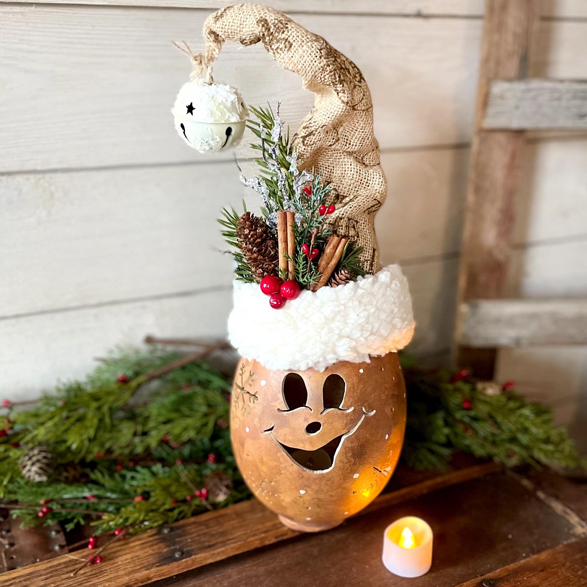 Decorative lantern with a face, surrounded by Christmas elements on a wooden surface.