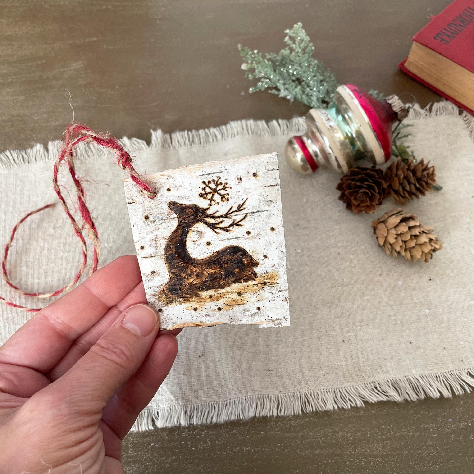 Hand holding a small wooden ornament with a reindeer design on a textured surface with decorative items.