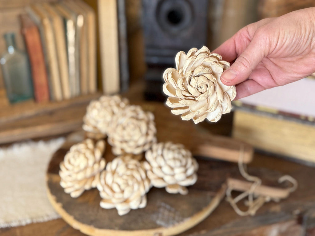 Hand holding a decorative pine cone with more pine cones on a wooden surface.