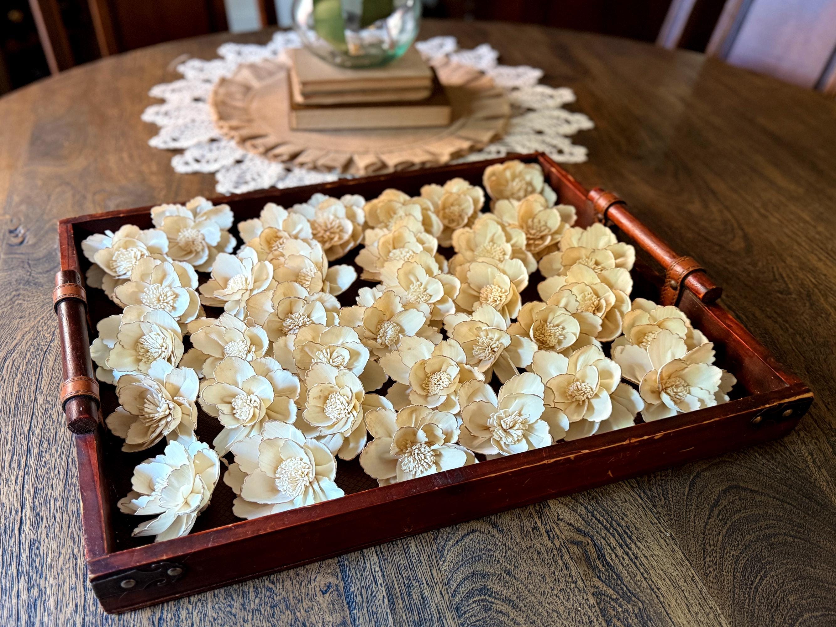 Decorative tray with beige floral arrangements on a wooden table.