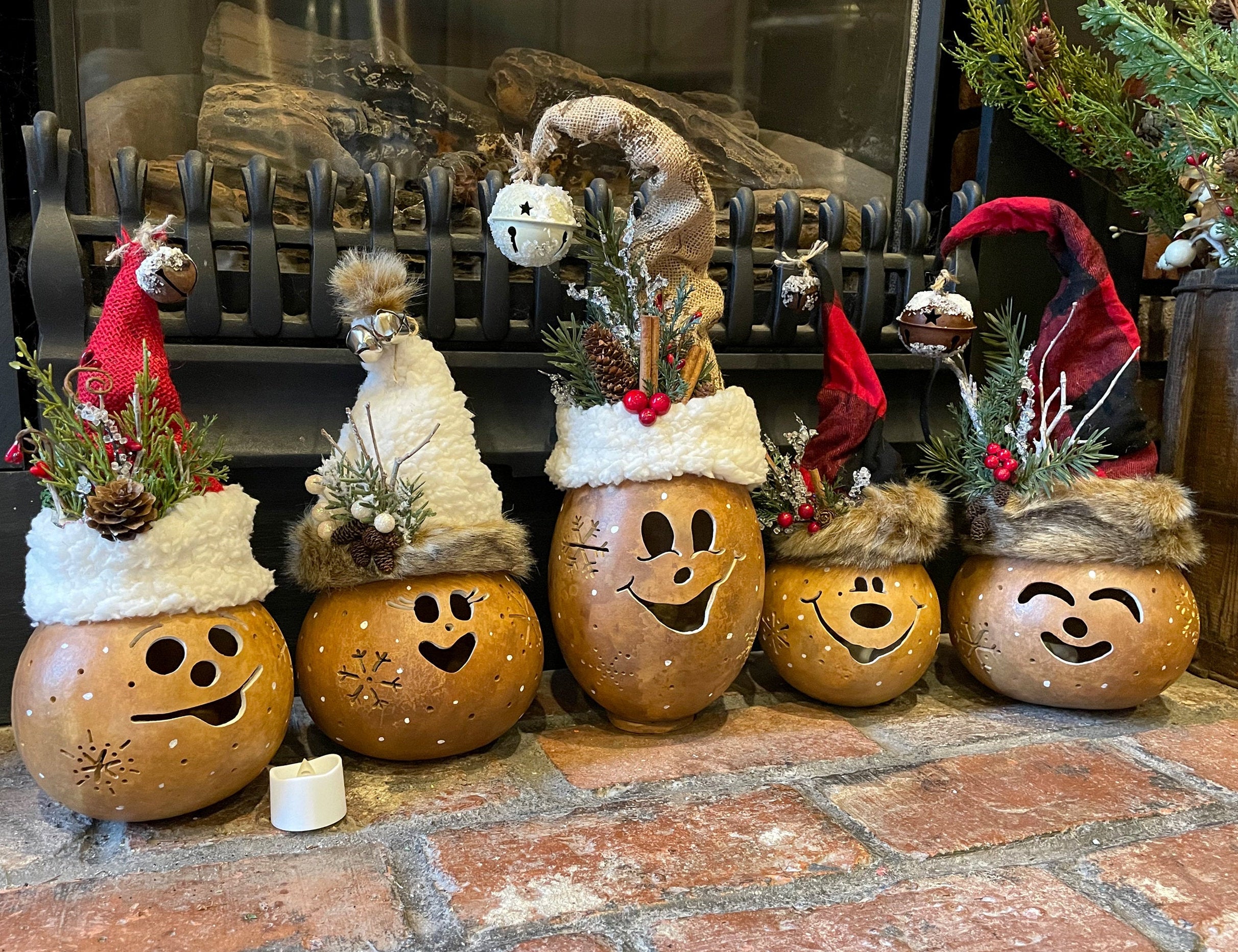 Decorative pumpkins with faces and Christmas hats on a stone surface in front of a fireplace.