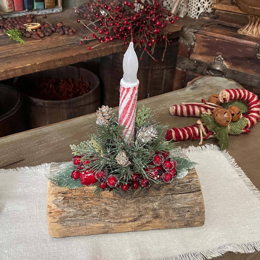 Decorative Christmas centerpiece with candle and berries on a wooden log, surrounded by festive decor.
