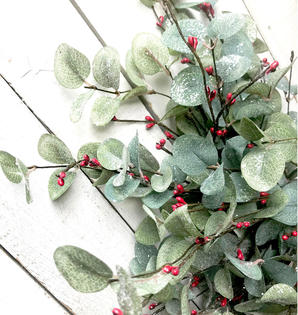 Decorative wreath with green leaves and red berries on a white wooden surface