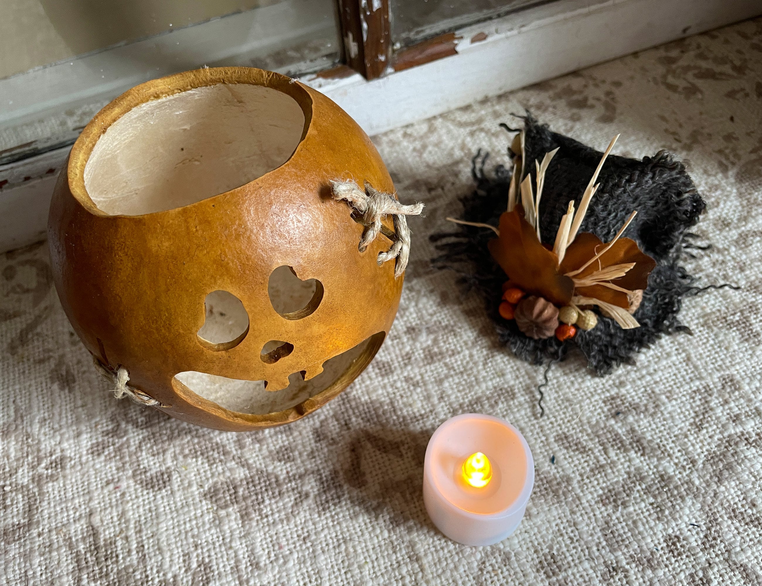 Decorative gourd with cut-out patterns next to a small candle on a textured surface.