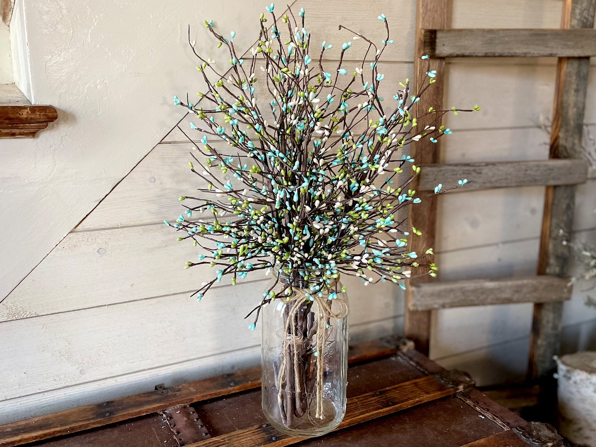 Decorative arrangement of branches with small lights in a glass jar on a wooden surface.