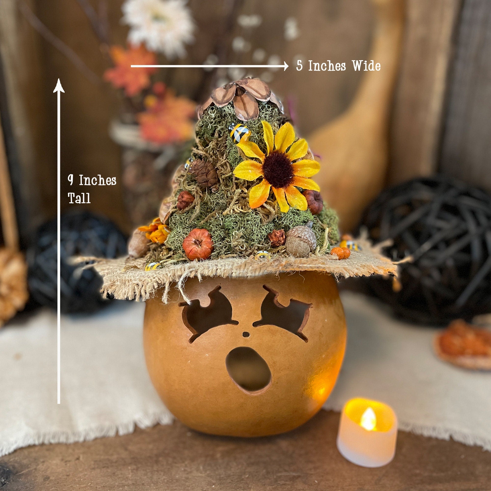 Decorative pumpkin with a small tree and sunflower on top, surrounded by autumn-themed decor.
