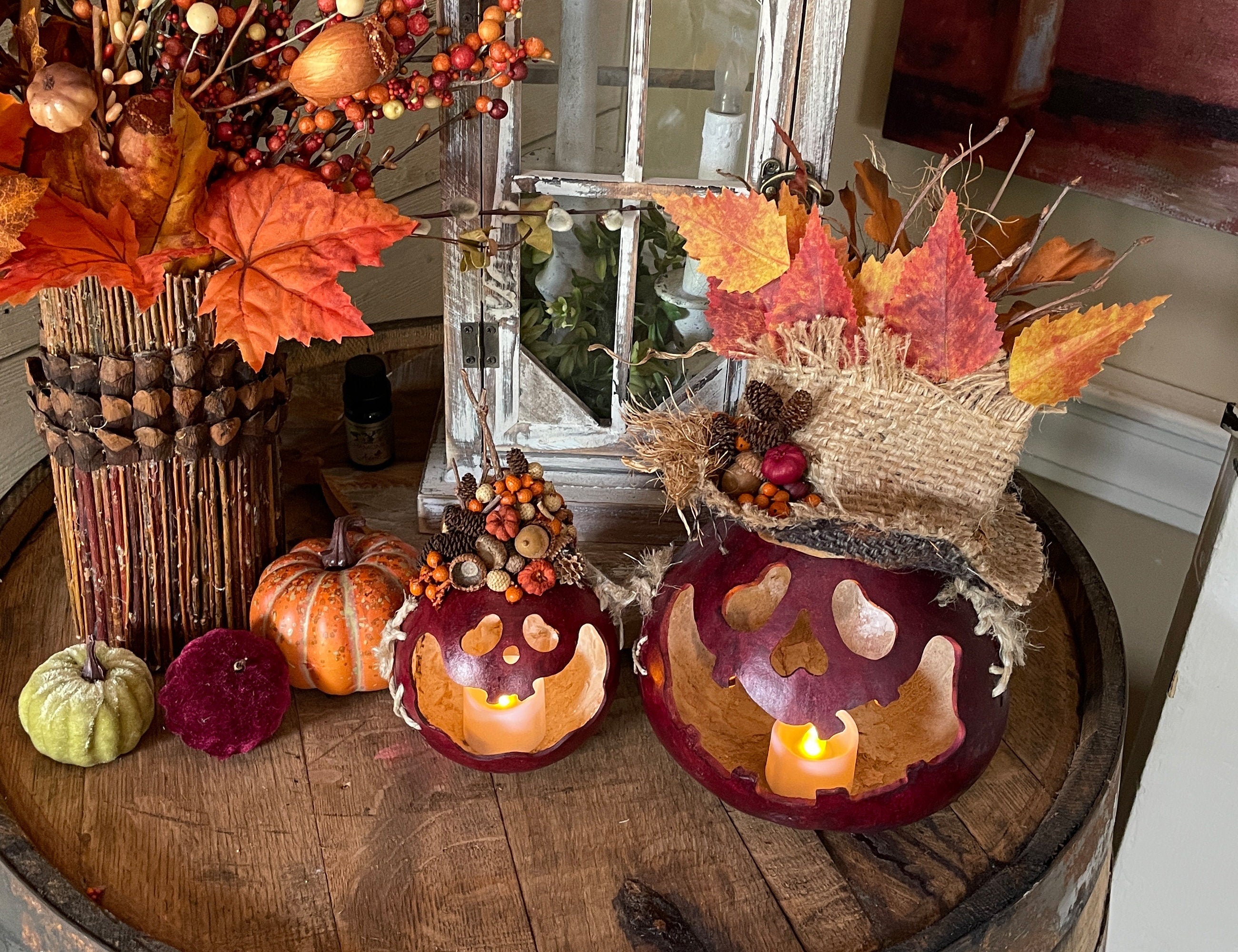 Decorative setup with pumpkins, candles, and autumn leaves on a wooden surface.