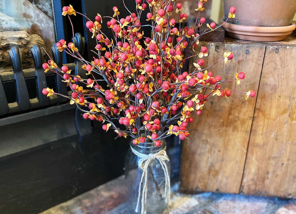 Bouquet of red and pink berries in a clear vase on a rustic wooden surface.