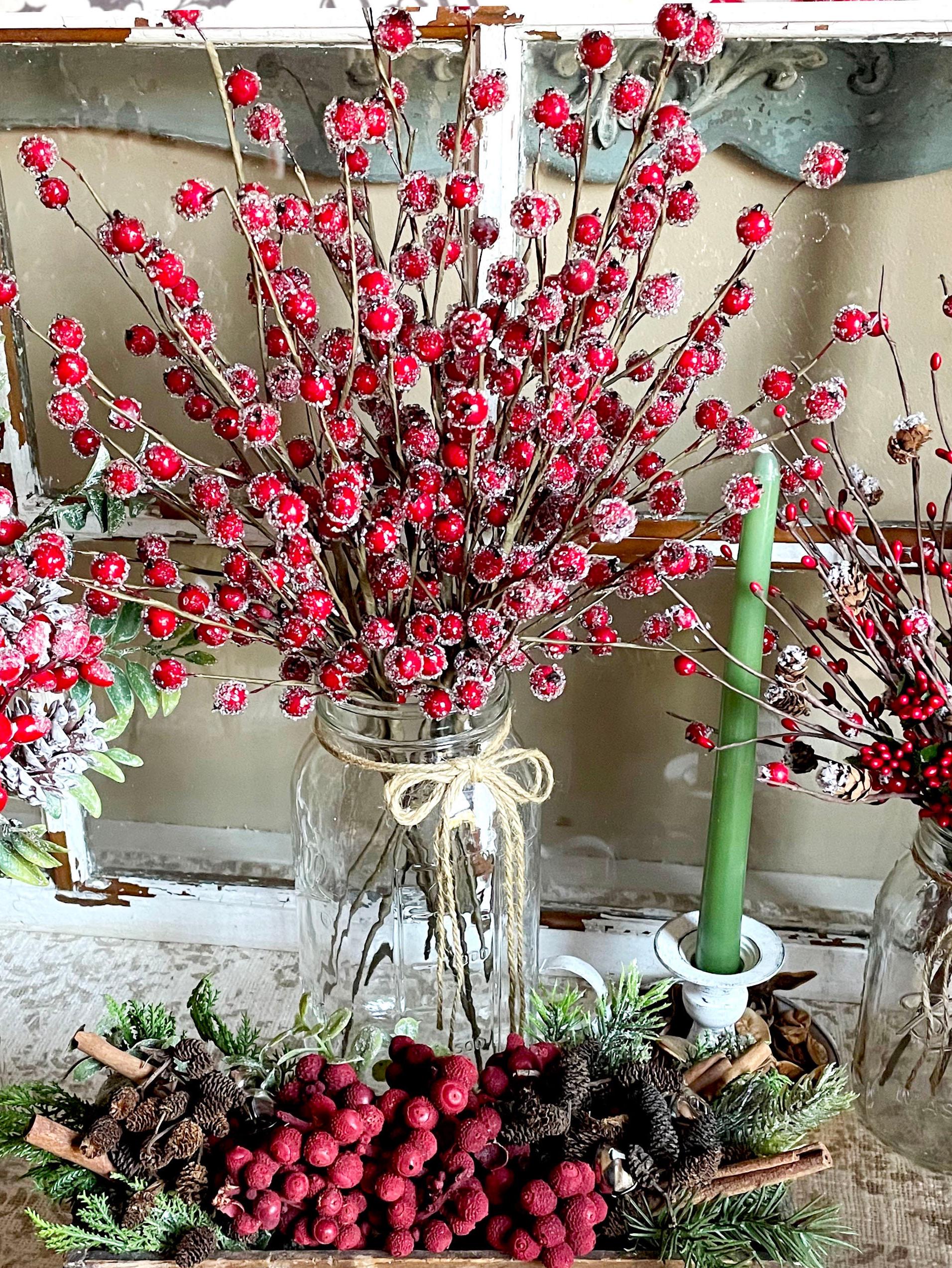 Decorative arrangement with red berries, green candle, and glass jars on a rustic surface.
