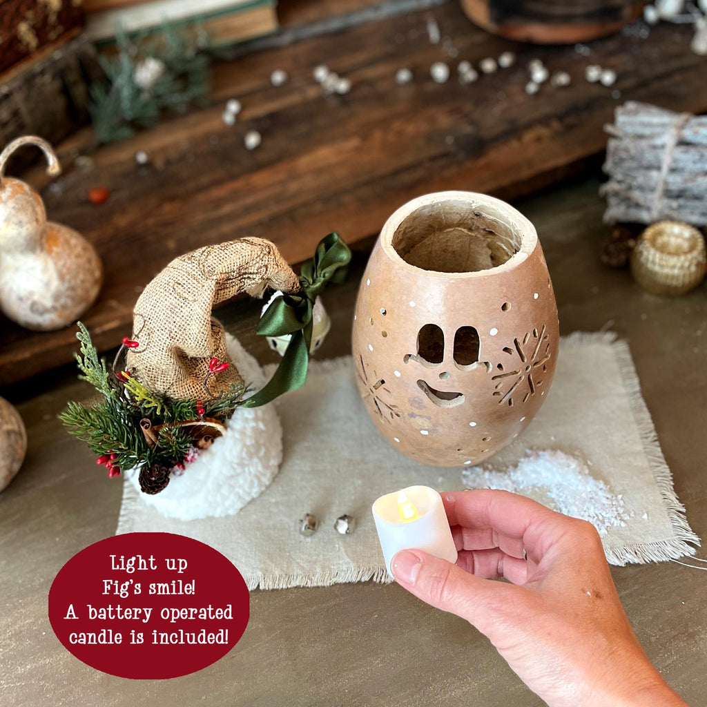 Decorative lantern with a smiling face, held by a hand with a battery-operated candle, on a rustic surface.