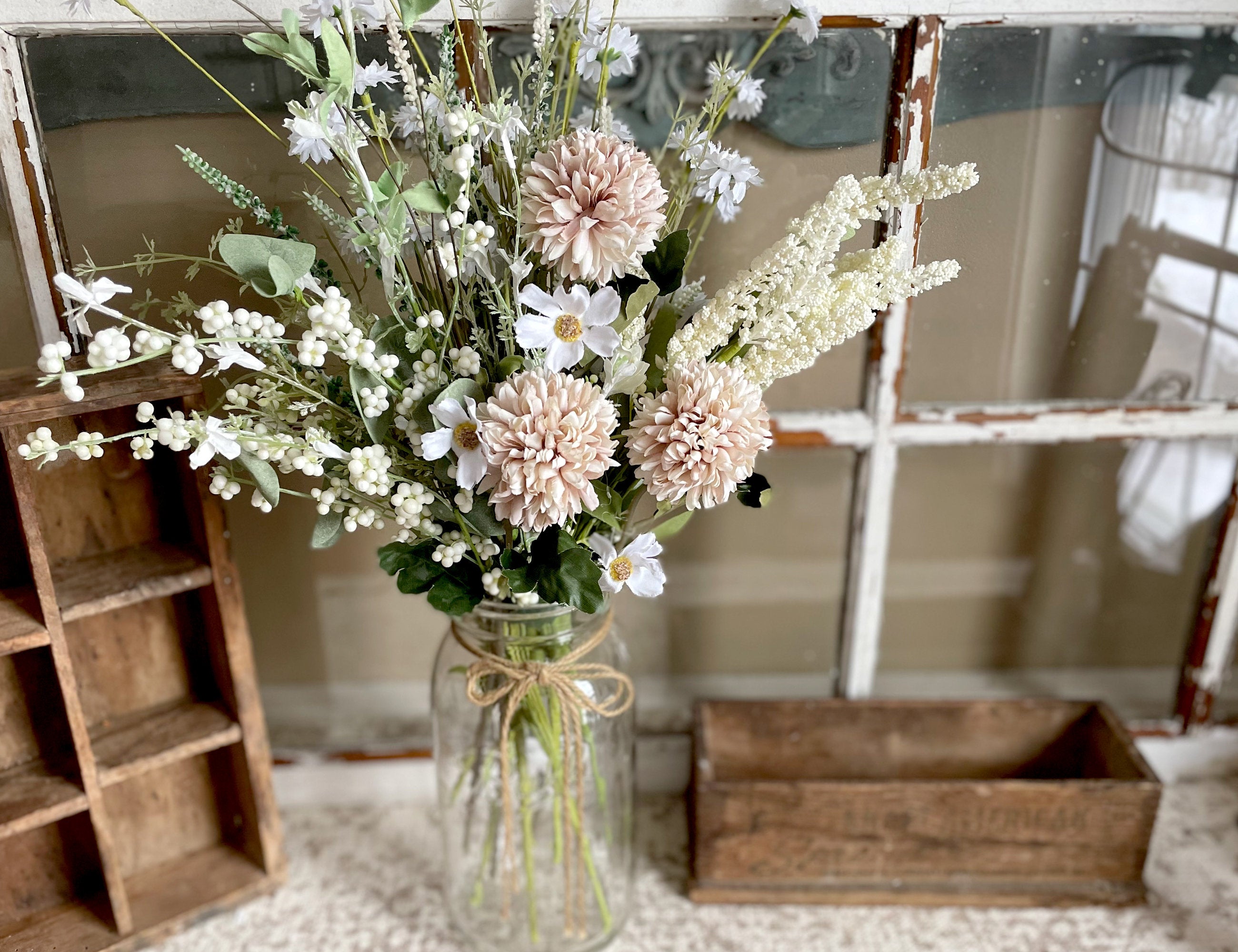 Bouquet of flowers in a glass jar on a surface with a wooden crate and mirror in the background.