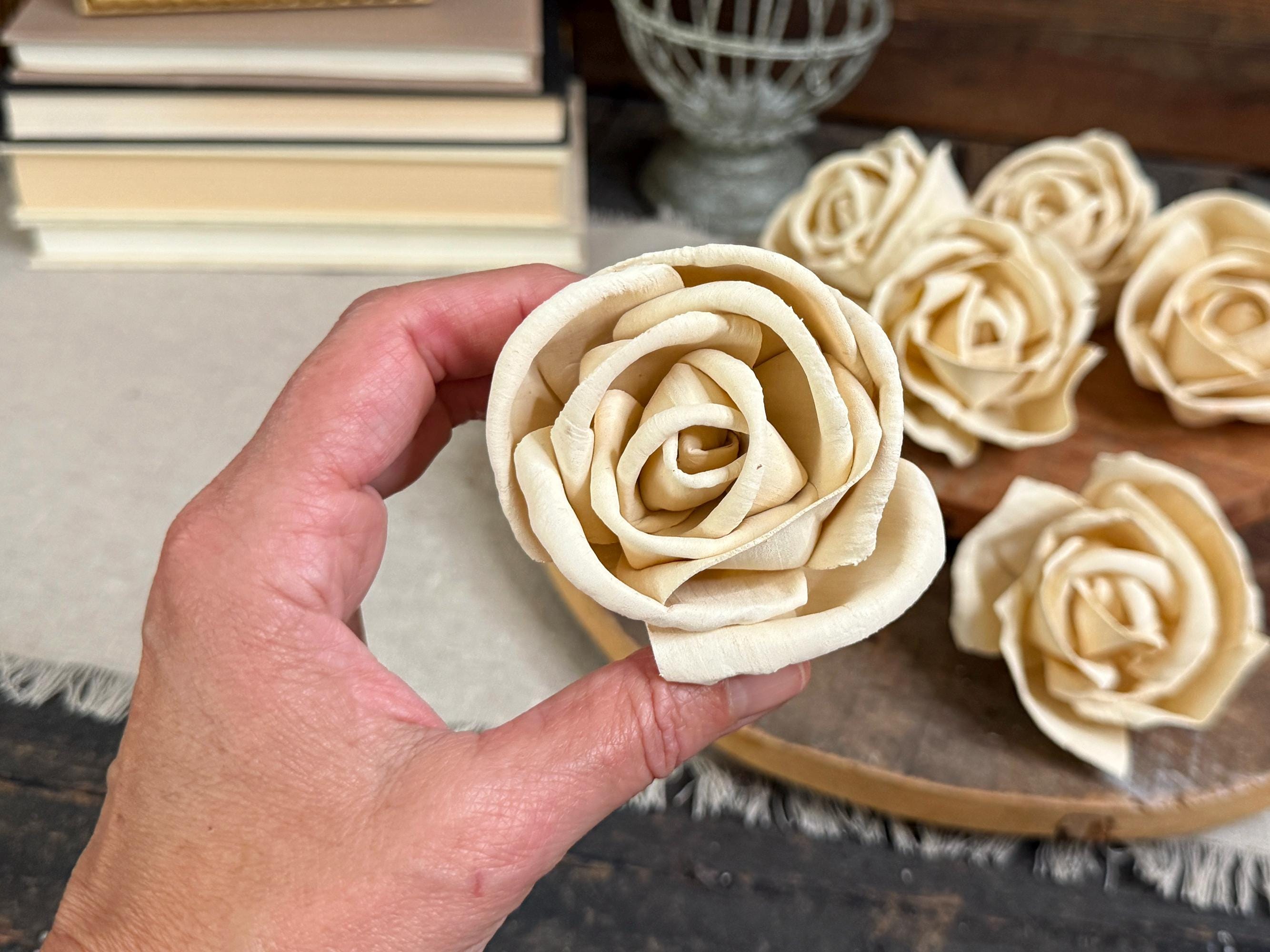 Hand holding a rolled dough rose with more roses on a wooden board in the background.