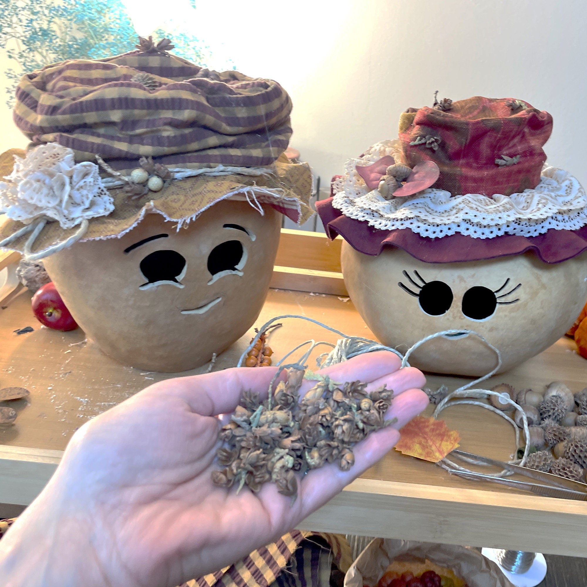 Two decorated pumpkins with faces and a hand holding dried flowers.