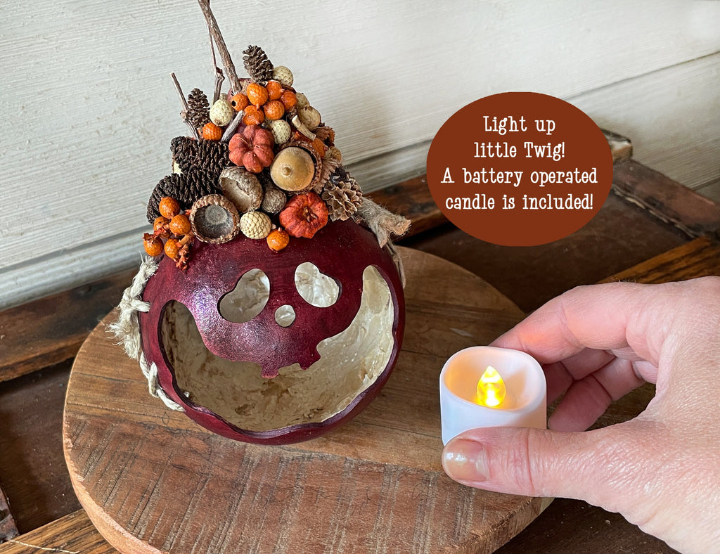 Decorative apple with autumn elements and a hand holding a battery-operated candle.