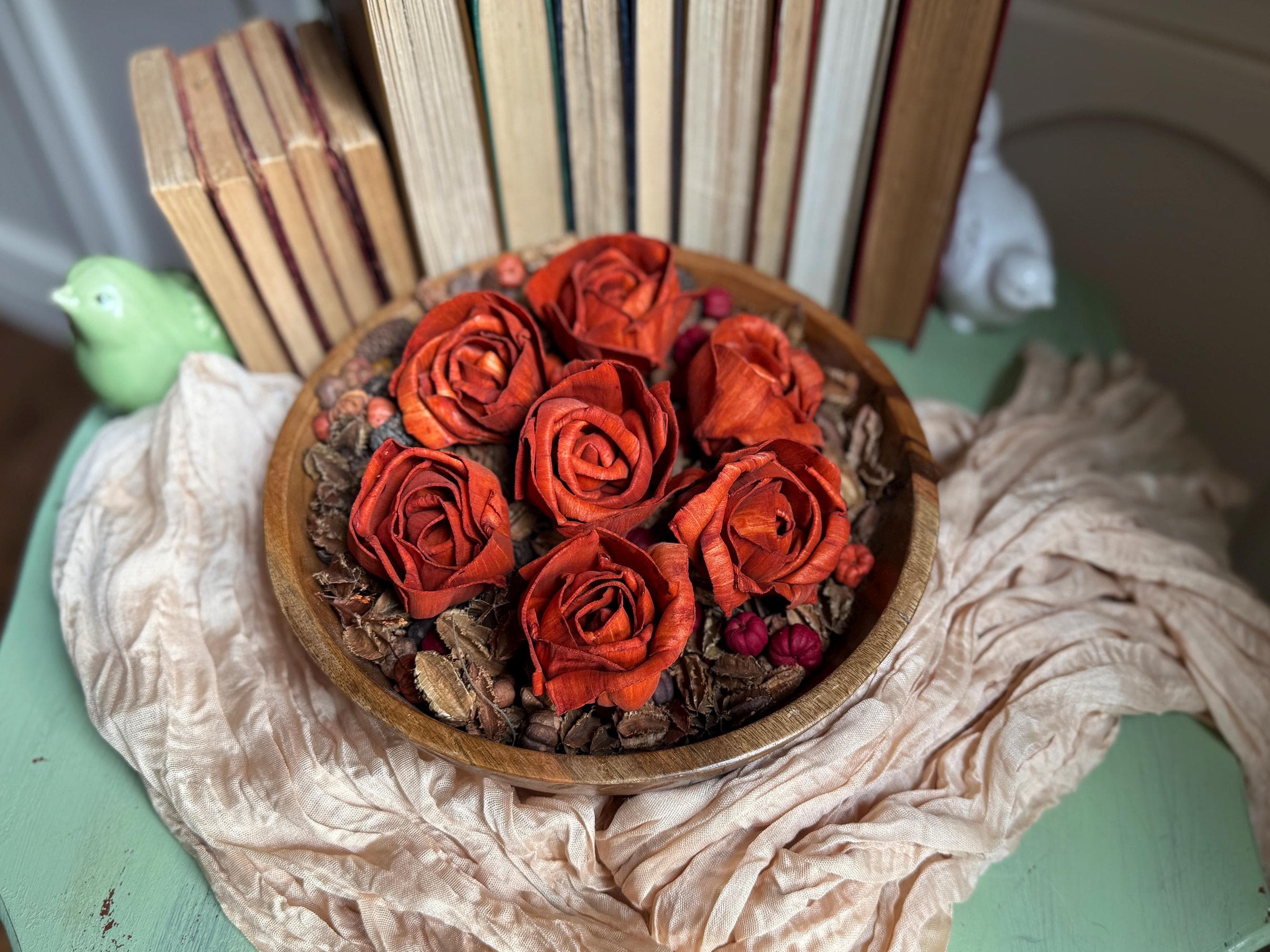 Wooden bowl with an orange rose arrangement on a textured surface with books in the background