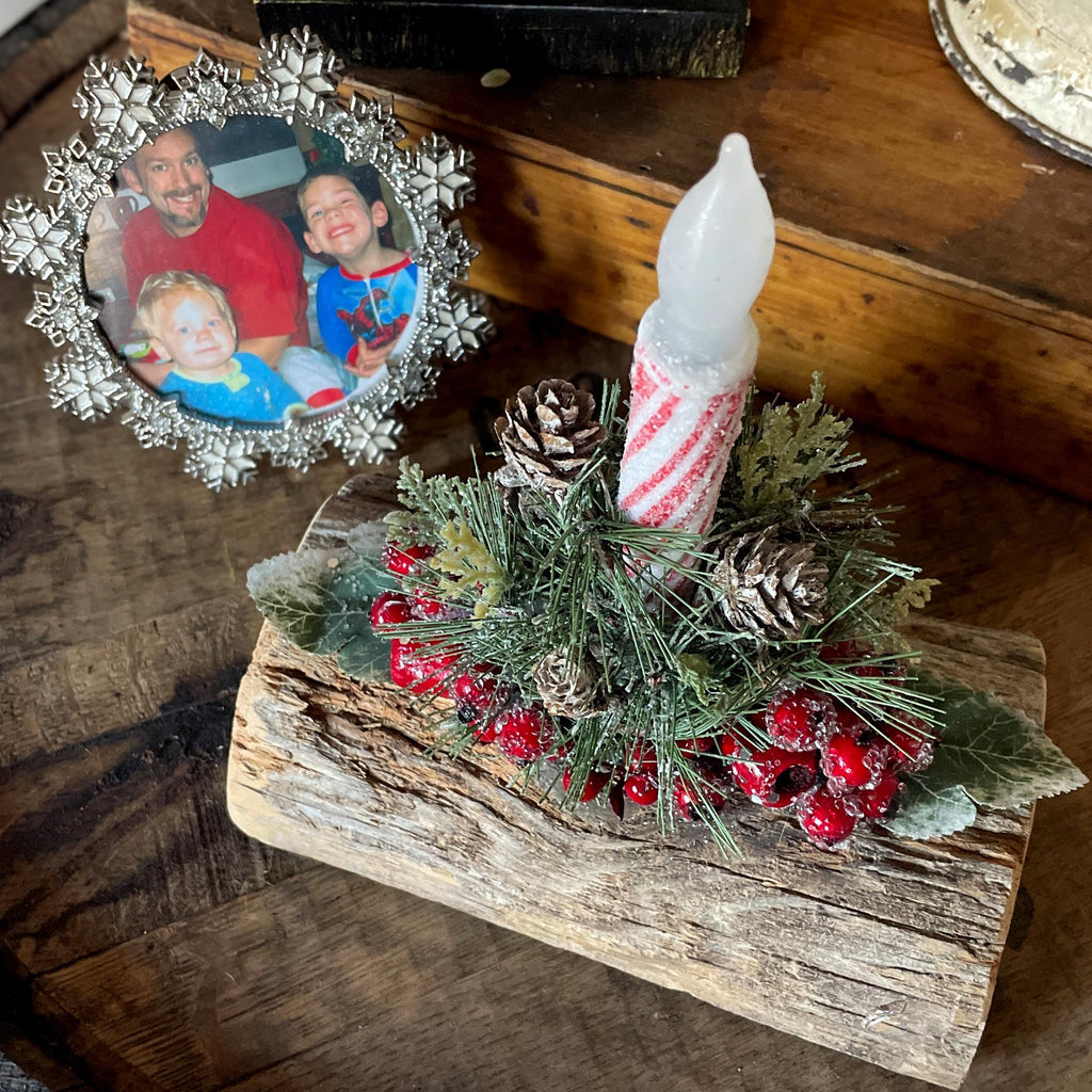 Decorative Christmas arrangement with a candle, pinecones, and berries on a wooden base.