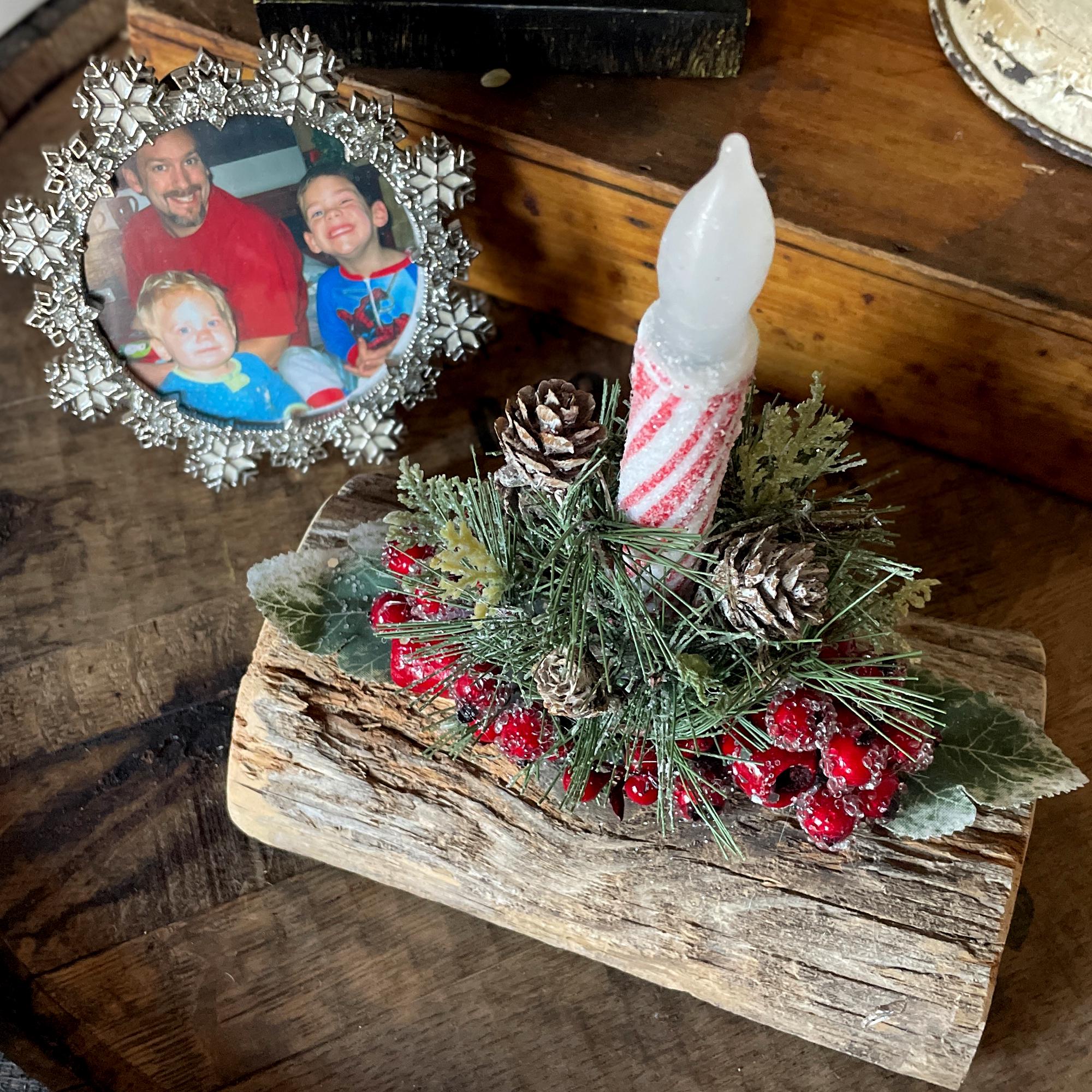 Decorative Christmas arrangement with a candle, pinecones, and berries on a wooden base.