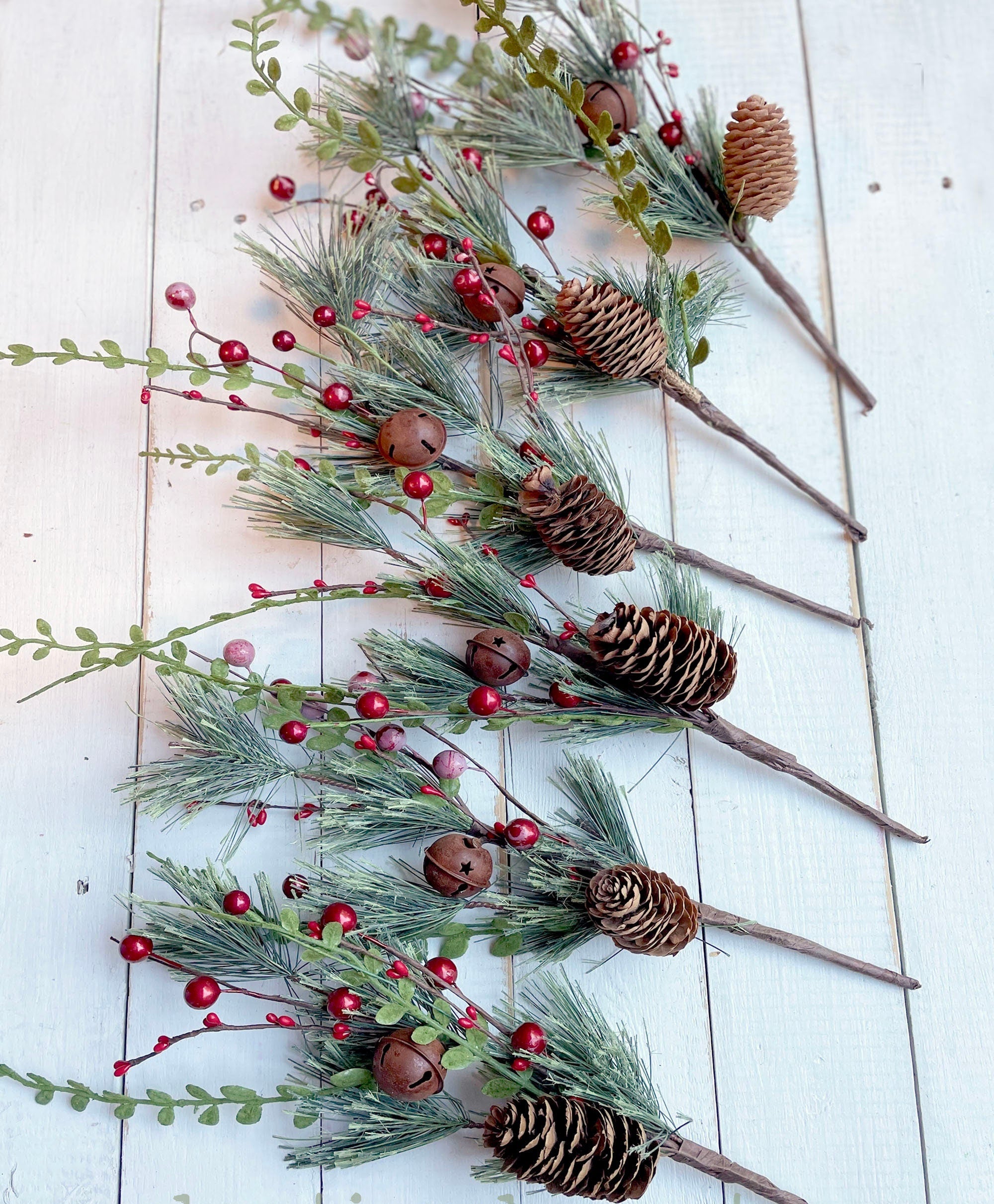 Decorative arrangement of greenery, pinecones, and berries on a white wooden surface with 'boutiquebarnetsy.com' branding.