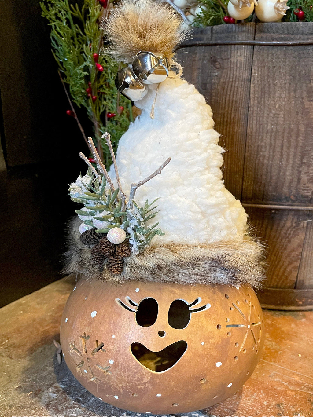 Decorative pumpkin with a face cutout, topped with a fluffy white angel figure, against a wooden background.