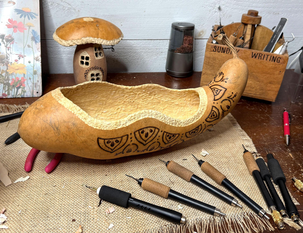elongated gourd shaped bowl with engraved patterns on a table with writing instruments.