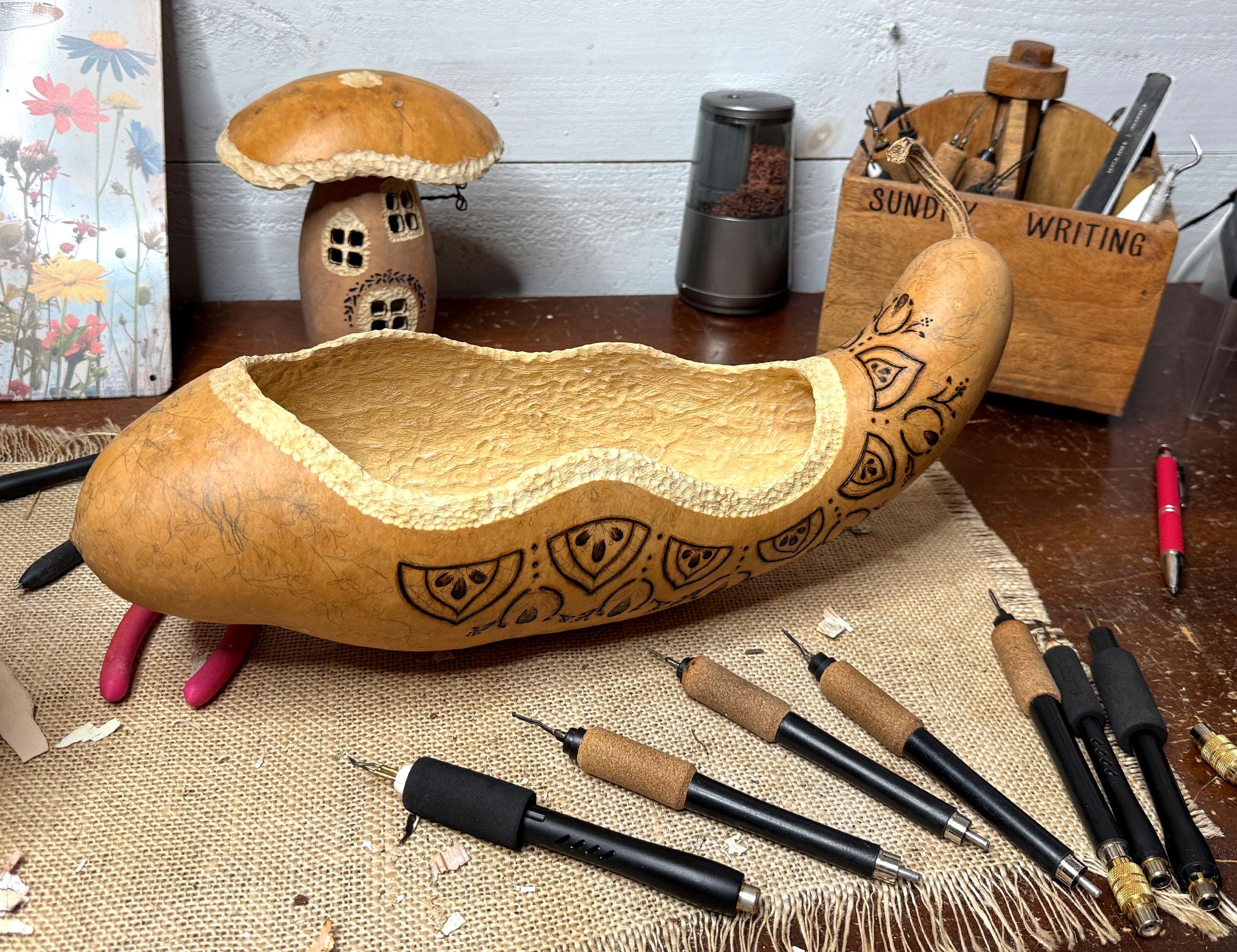 elongated gourd shaped bowl with engraved patterns on a table with writing instruments.