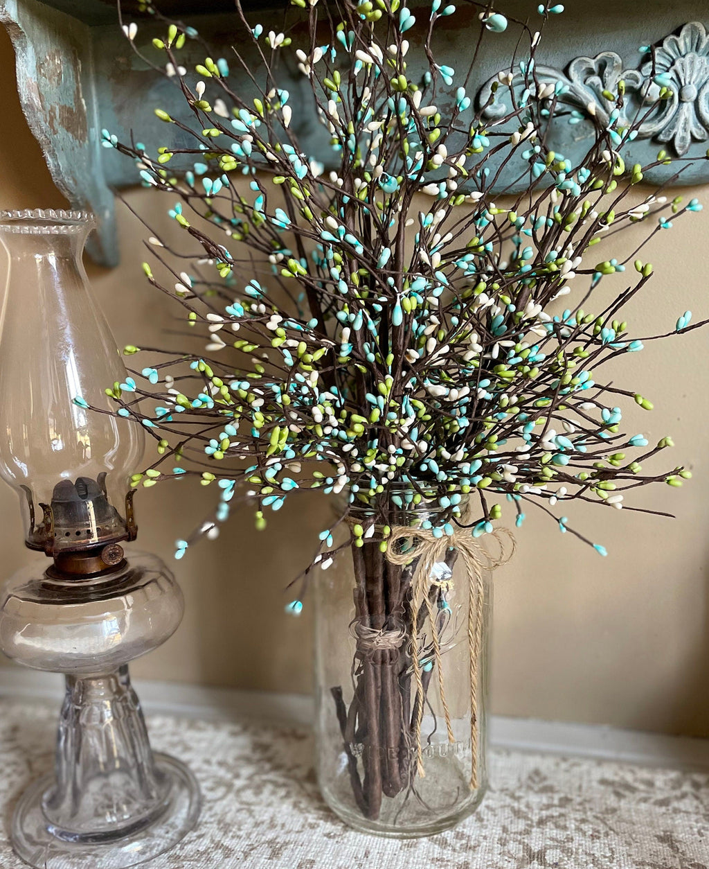 Decorative arrangement of branches in a glass jar with an oil lamp in the background.