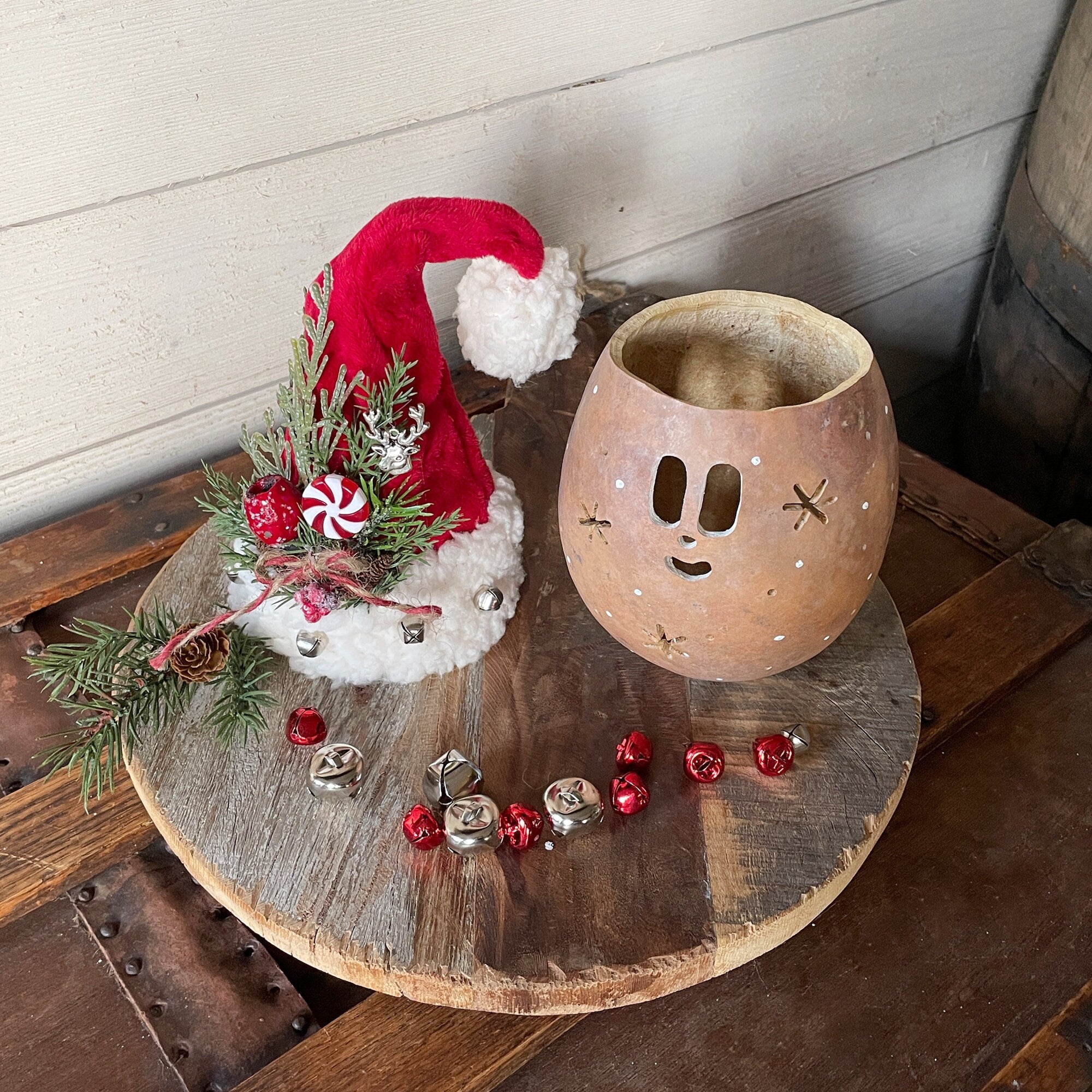 Decorative items including a small tree with a red hat, a ceramic lantern, and small red and silver ornaments on a wooden surface.