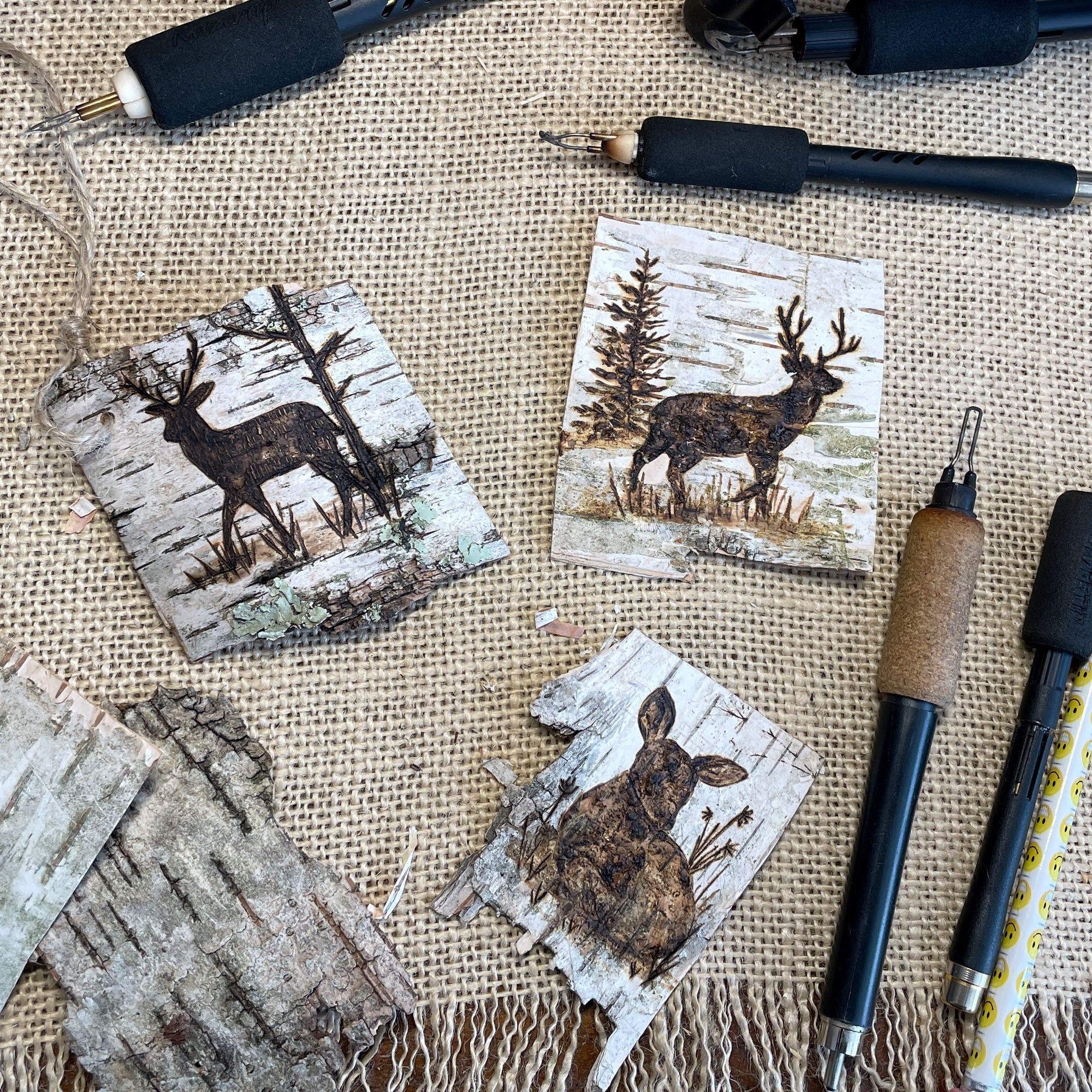 Wooden birch bark present toppers with deer  designs on a textured surface with pyrography tools.