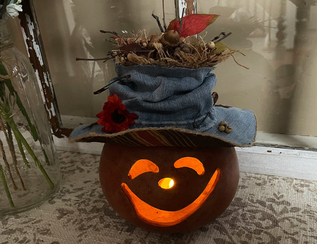 Pumpkin with a jack-o'-lantern face, denim hat, and decorative elements on a textured surface.