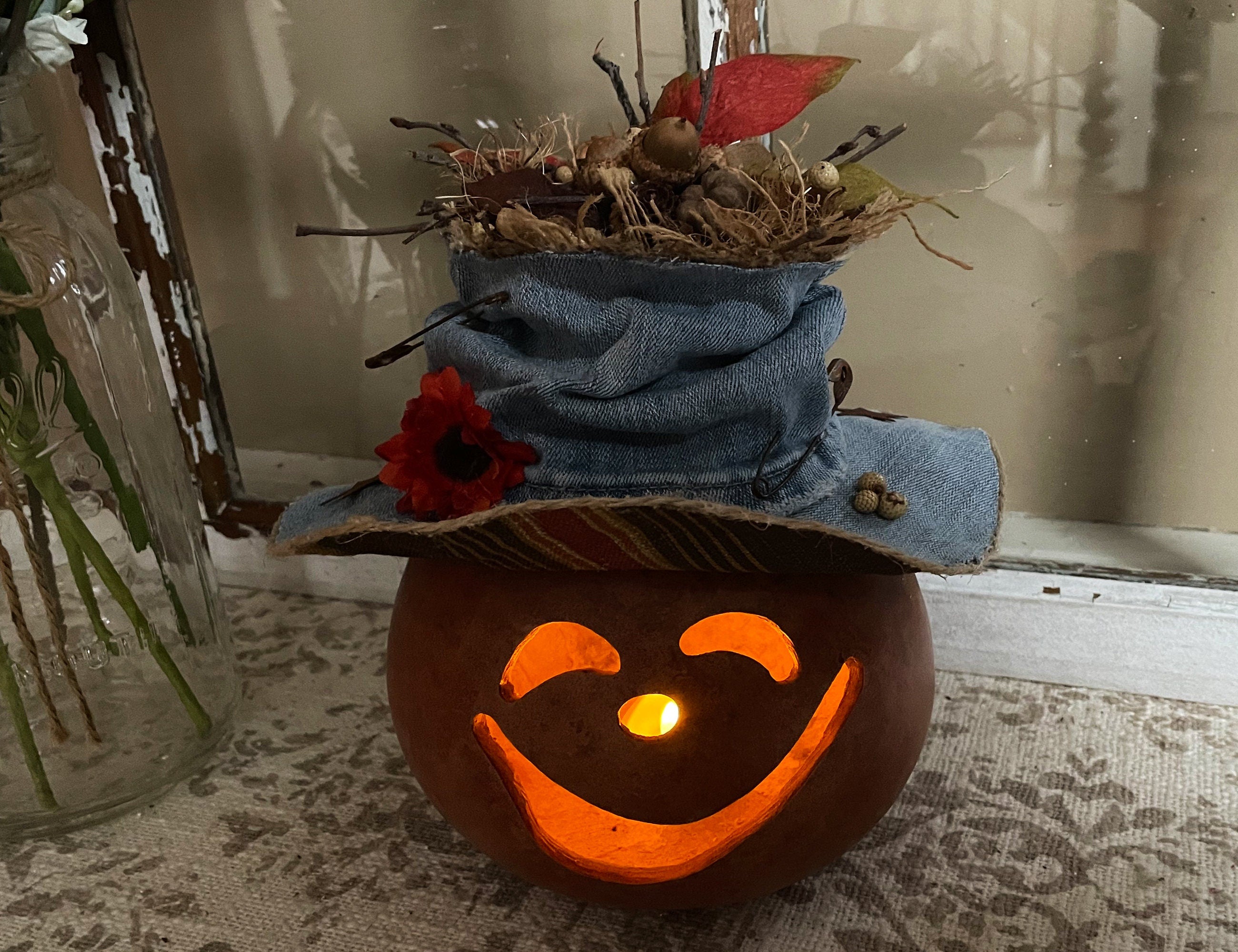 Pumpkin with a jack-o'-lantern face, denim hat, and decorative elements on a textured surface.