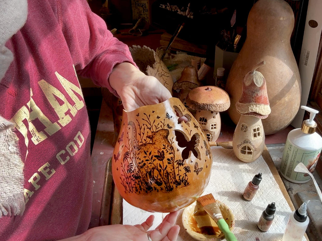 Person holding a gourd with carved designs in a workshop setting