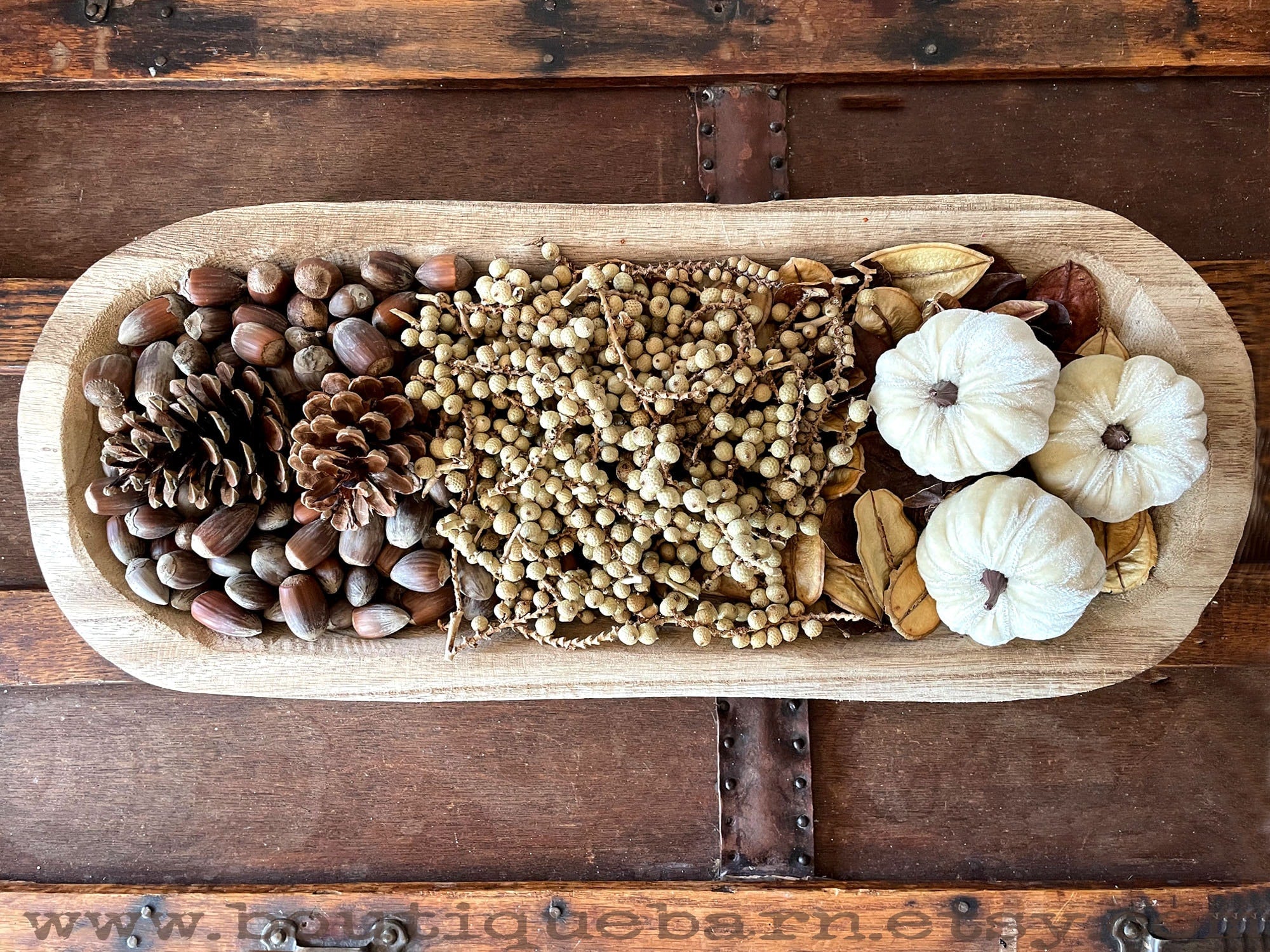 Wooden tray with pinecones, dried berries, and small pumpkins on a rustic wooden background.