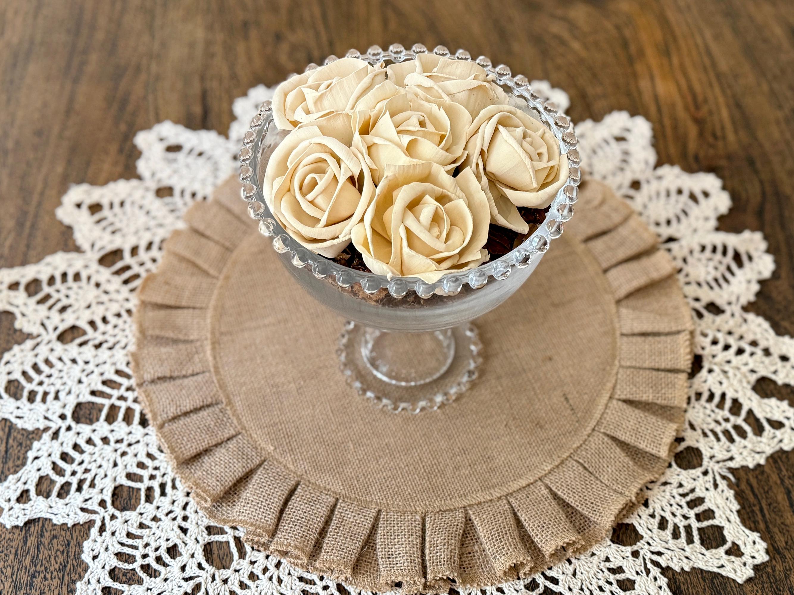 Decorative arrangement of cream-colored roses in a glass vase on a burlap mat with lace doily