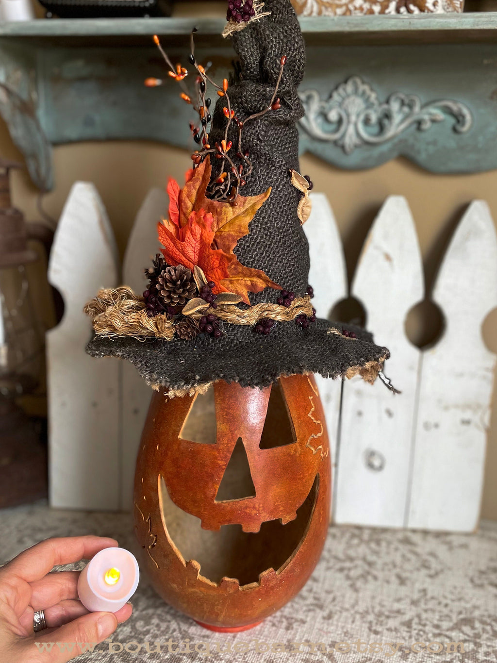 Decorative Halloween pumpkin with a witch hat and autumn leaves, held by a hand.