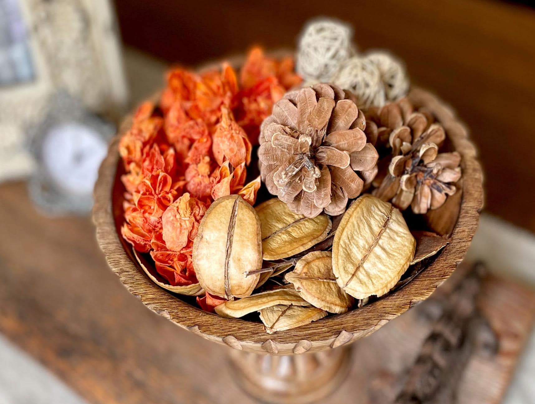 Decorative bowl with dried flowers and pinecones on a wooden surface