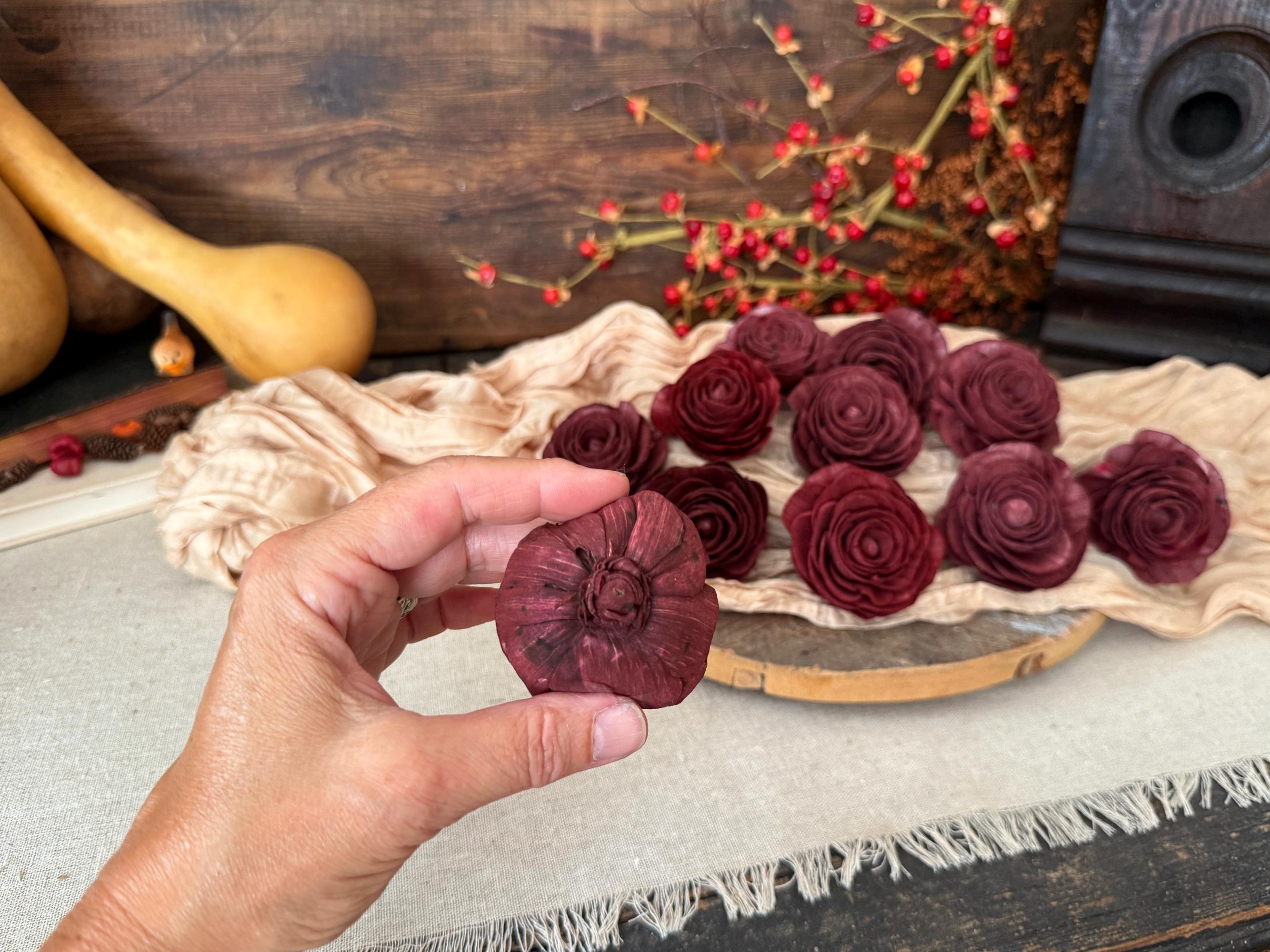 Hand holding a red wood flower blossom.  A wooden surface and decorative items in the background