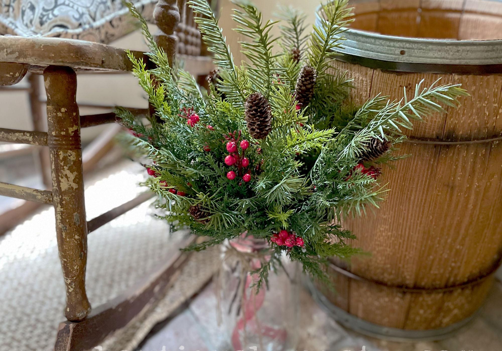 Decorative Christmas arrangement with greenery and berries in a glass vase on a wooden table.