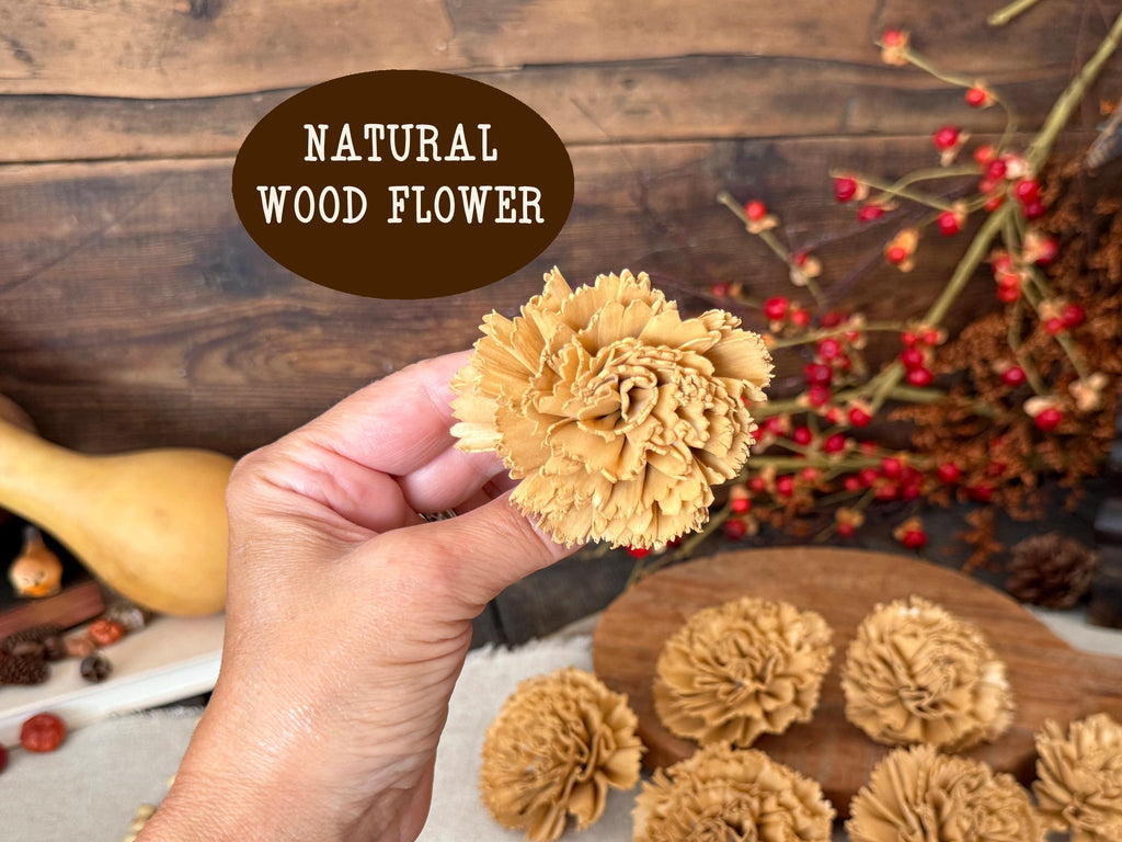 Hand holding a natural wood flower with more flowers on a wooden surface.