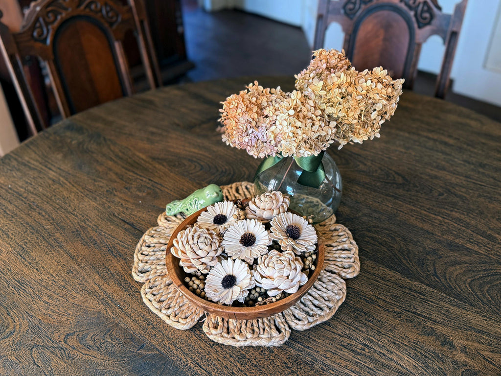 Decorative flower arrangement in a vase on a wooden table with a doily and small container.